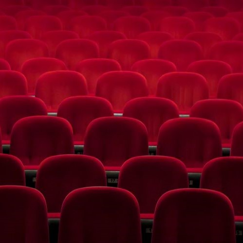 Several rows of cinema chairs upholstered in red velvet.