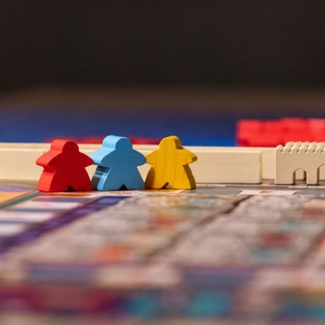 Three wooden meeples (red, blue and yellow) on a Merv board game.